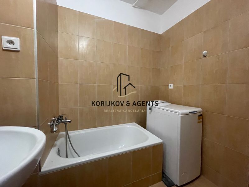Bathroom with a bathtub and a washing machine in a 2-room apartment. Tiled walls, white sanitary equipment.