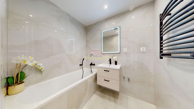 Bathroom with a bathtub, sink, and illuminated mirror in a 3-room apartment.