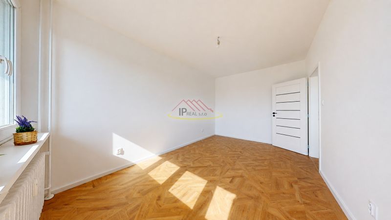 A spacious room in a 3-room apartment with a wooden decor floor and white walls.