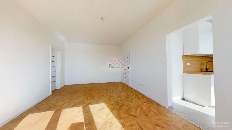 A white room with a wooden decor floor, entrance to the kitchen in a 3-room apartment.