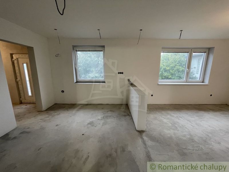 An unfloored interior of a family house with two windows and a door.