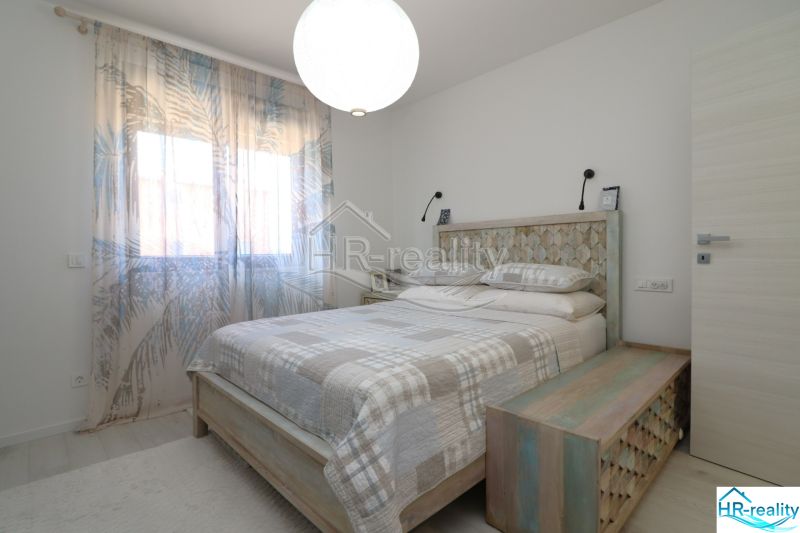 Bright bedroom with a double bed in a holiday apartment, light curtains, and a decorative floor.