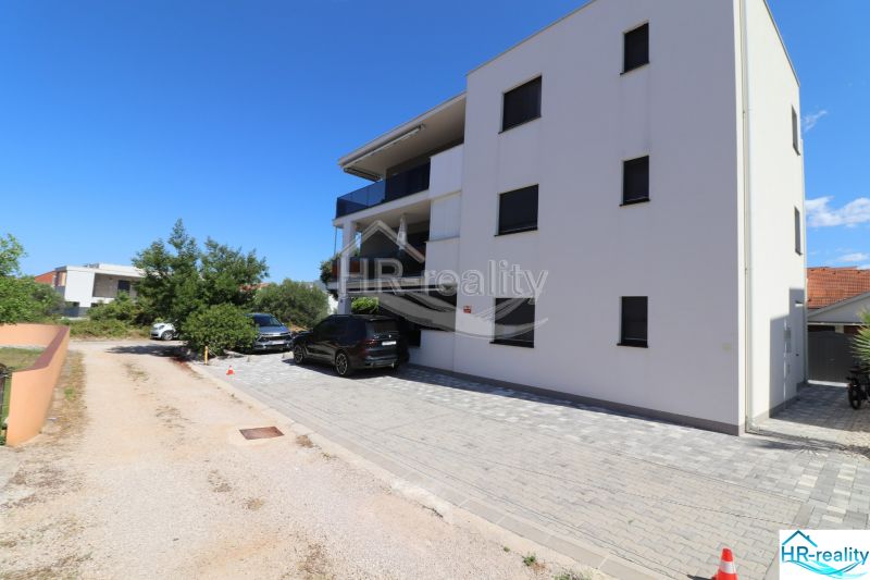 The exterior of a holiday apartment in Srima with two parked cars and a blue sky.