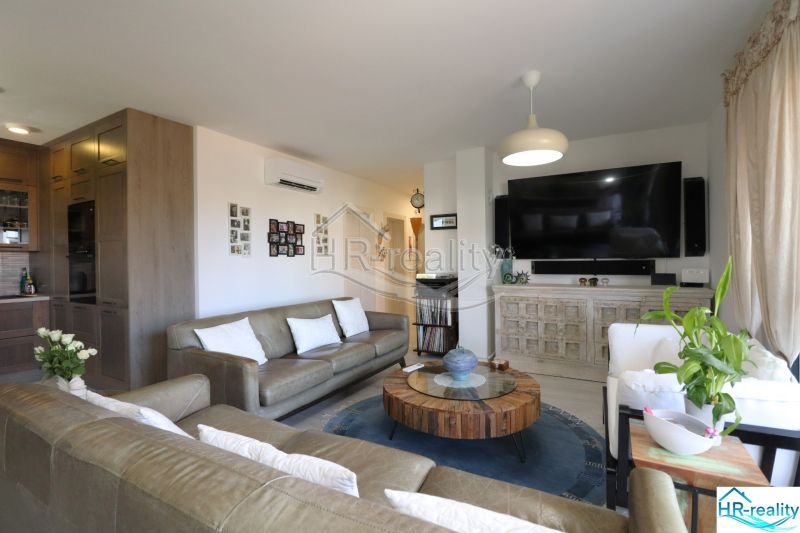 In the recreational apartment, there is a living room with a sofa, a television, and a floor with a wooden decor.