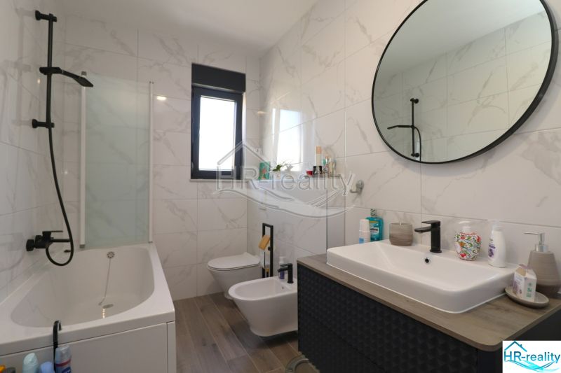 Bathroom in a holiday apartment with a bathtub and a sink, floor with wooden decor.