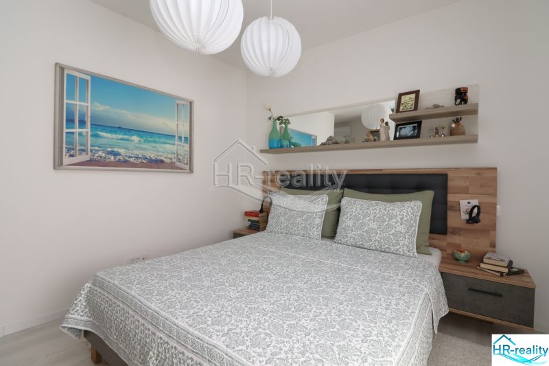 Bedroom in a holiday apartment with a painting by the sea and a shelf above the bed.
