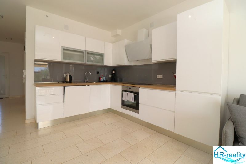 A kitchen in a holiday apartment with white cabinets and appliances, and a wooden decor floor.