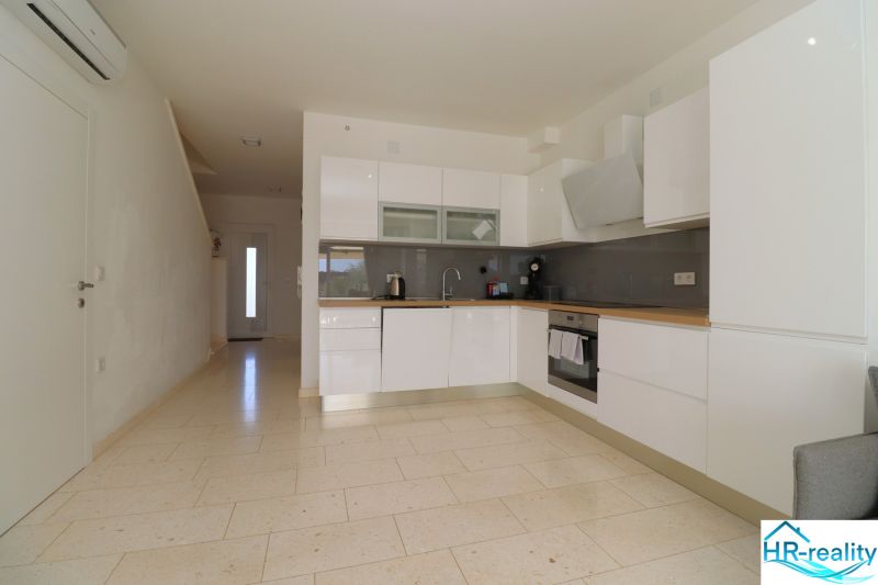 A kitchen in a holiday apartment with white cabinets and a light wooden-decor floor.