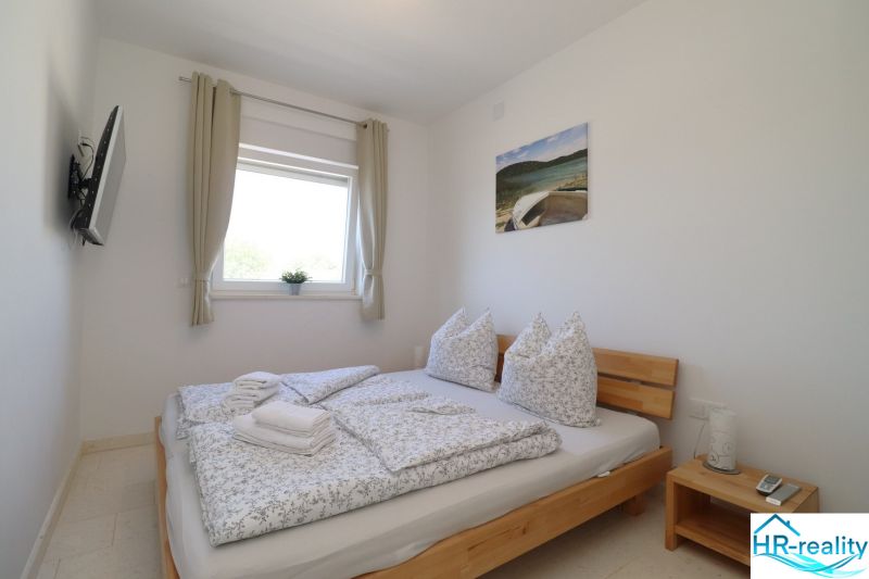 Bright bedroom in a holiday apartment with a double bed and a TV on the wall.