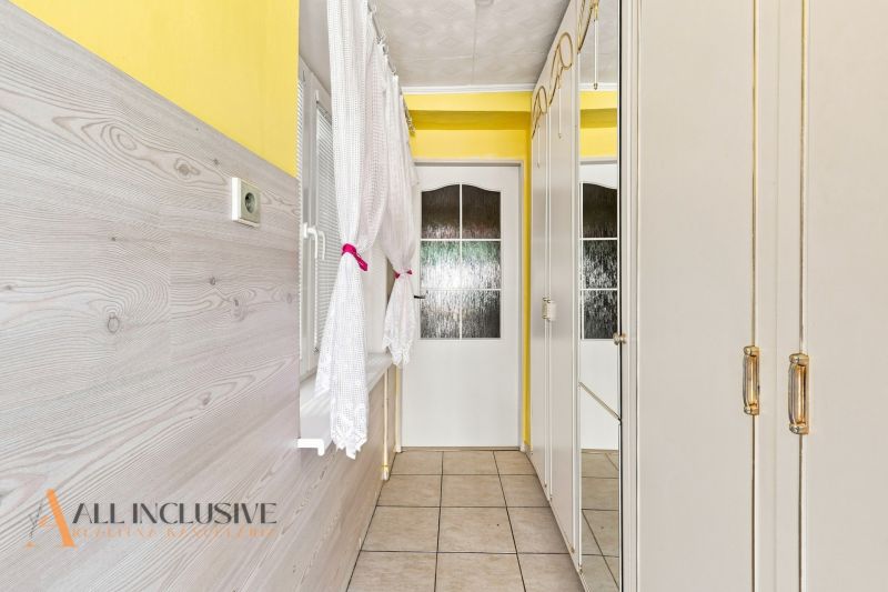 A hallway with a yellow wall, white furniture, and a window in a family house.