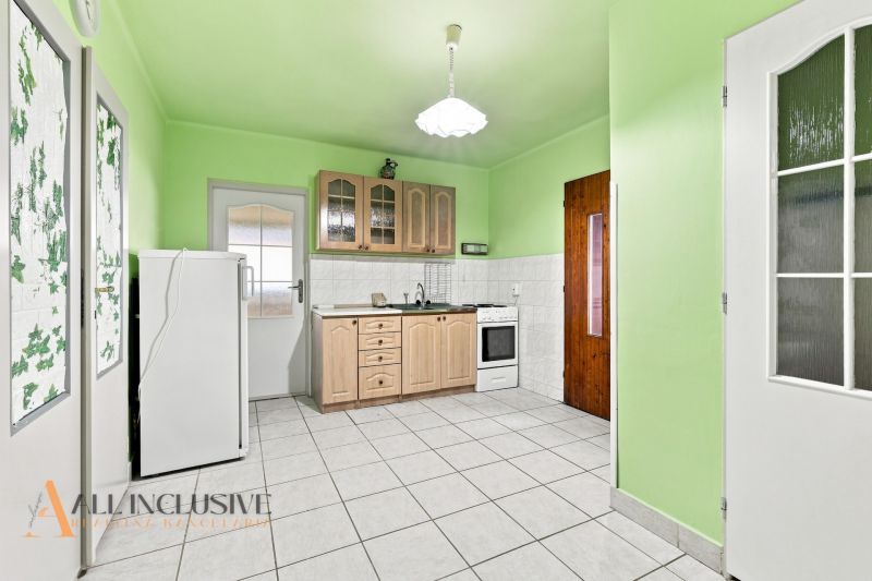 A kitchen in a family house with light green walls, tiles, and a wooden kitchen unit.