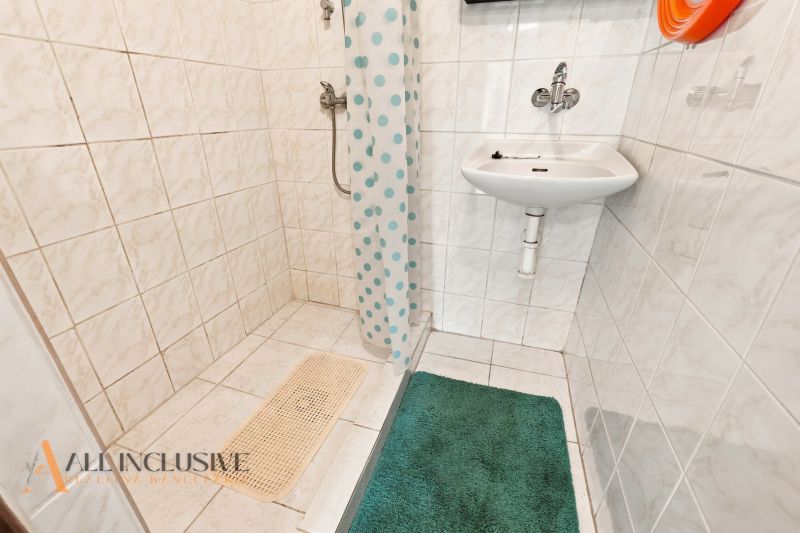 A bathroom in a family house with a sink and a shower, tiled with white tiles.