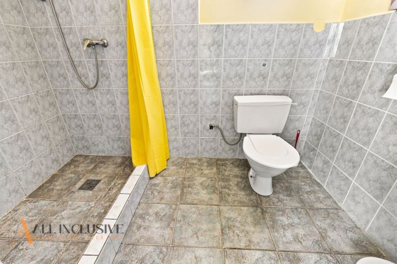 Bathroom with a toilet, shower, and yellow curtain in a family house.