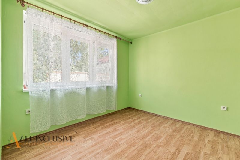 A room with a window, green walls, and a wooden-patterned floor in a family house.