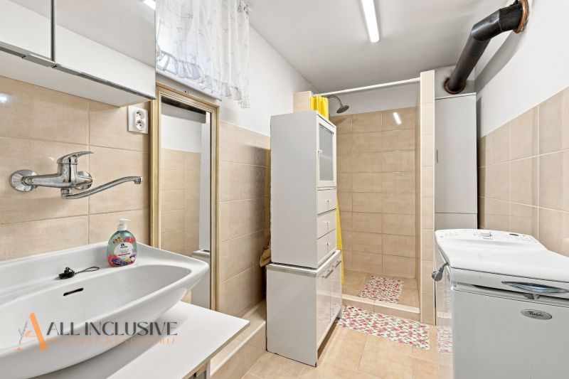 Bathroom with a sink, shower, and washing machine in a family house, with tiles and light-colored tiles.