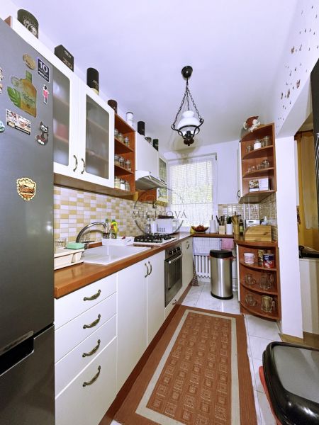 A kitchen in a 4-room apartment with white cabinets, a stove, a refrigerator, decorative tile.