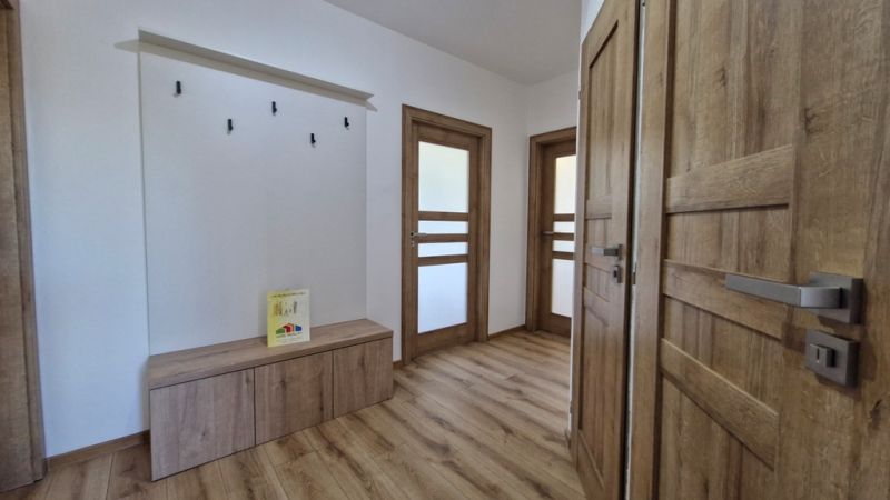 Interior of a 3-room apartment with a wood-patterned floor, wooden doors, and a coat rack.