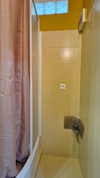 A shower corner in the bathroom of a 3-room apartment with beige tiles and a curtain.