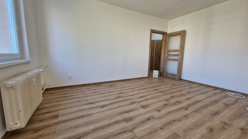 A room with a wooden decor floor, white walls, and doors in a 3-room apartment.