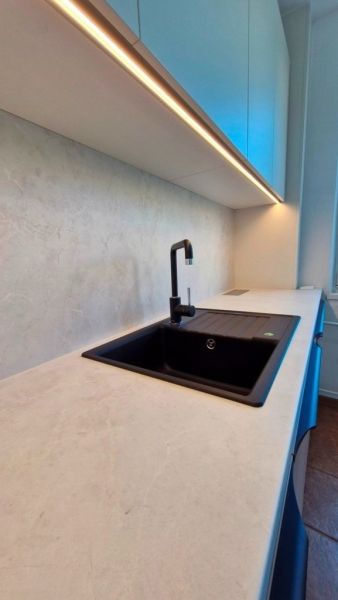 A kitchen in a 3-room apartment with a white countertop and a black sink.
