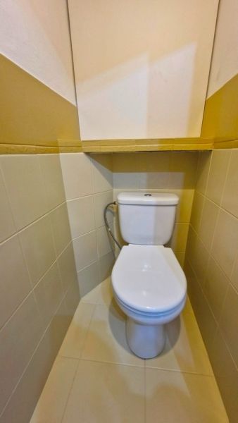 A toilet in a 3-room apartment with simple tiles and a back-tank toilet.