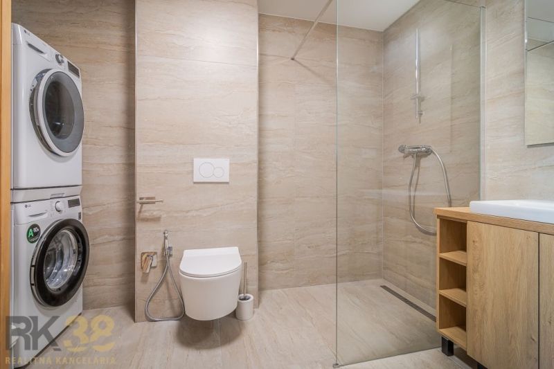 Bathroom with a shower and a washing machine in a 4-room apartment with a wooden decor floor.