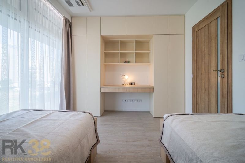 A room in a 4-room apartment with shelves, a table, and beds, flooring with a wood decor.