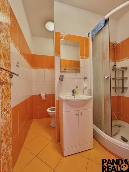 A bathroom in a one-room apartment with orange and white tiles and a shower corner.