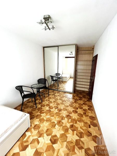 Bedroom with wood-patterned flooring in a 3-room apartment; bed, wardrobe, table, chairs.