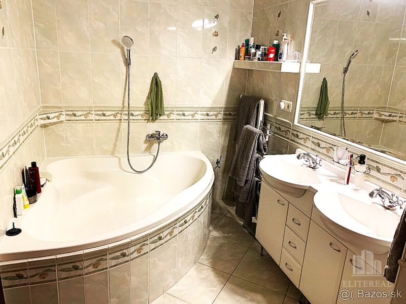 A bathroom with a corner bathtub and double sink in a three-room apartment.