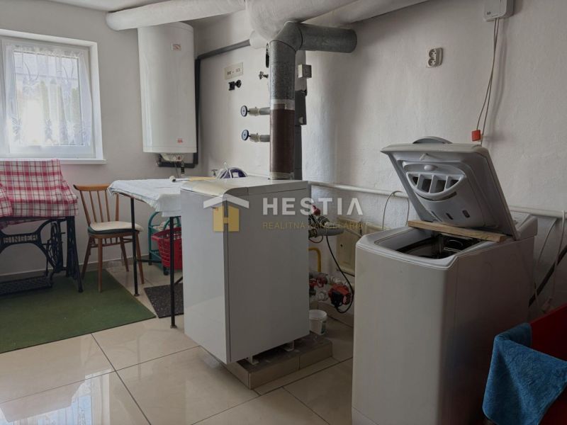 Laundry room in a family house with a washing machine, table, and water heating boiler.