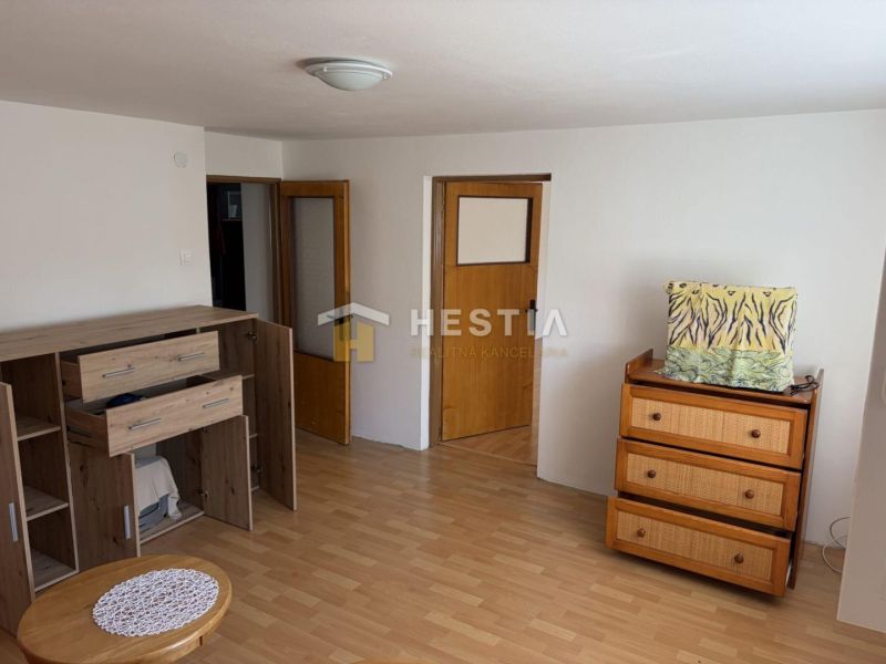 A room in a family house with furniture, a wooden decor floor, and white walls.