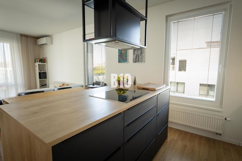 A kitchen in a 3-room apartment with a wooden decor floor and black cabinets.