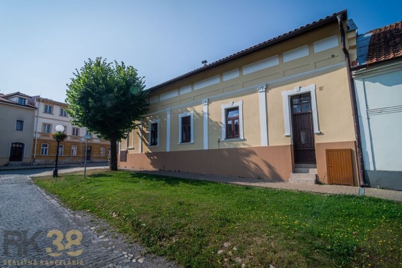 The building on Castle Square in Kežmarok surrounded by greenery and historical architecture.