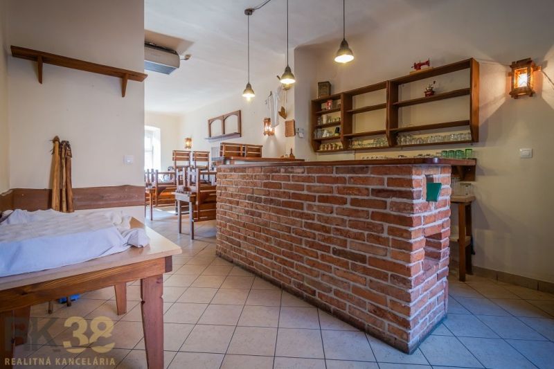 Interior of a gastro space with a brick bar, wooden chairs, and a tiled floor.
