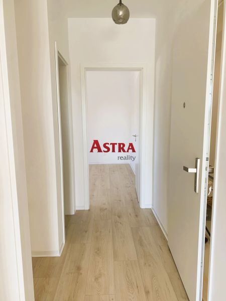 A hallway with white walls and a wooden decor floor in a 3-room apartment.