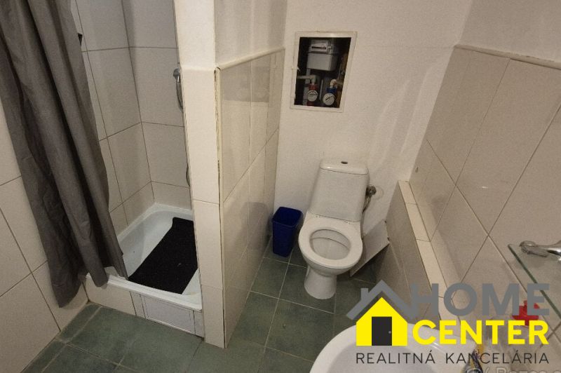 Bathroom with a shower in a studio apartment with a toilet and tiles.