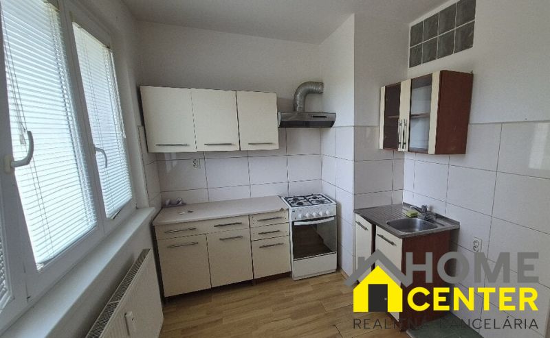 A kitchen in a one-room apartment with a wood-patterned floor and white cabinets.