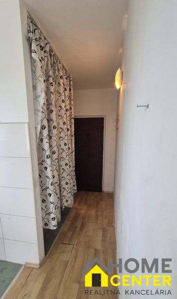 A narrow hallway with a wooden decor floor and a patterned curtain in a studio apartment.