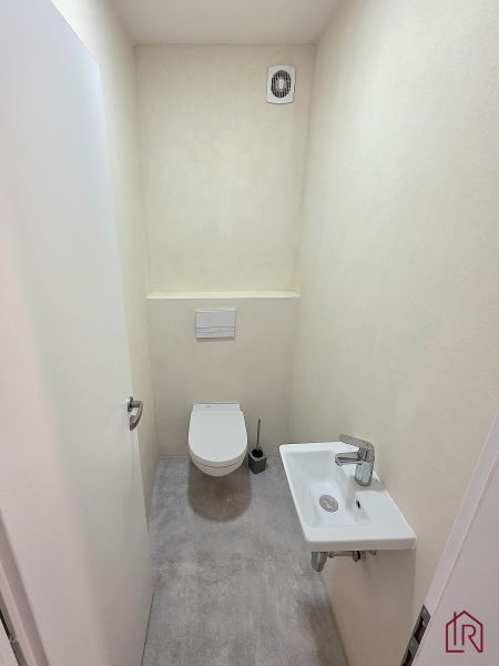 A toilet in a 2-room apartment with a fan and a small sink.