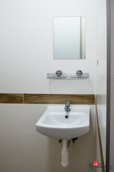 A bathroom in a studio apartment with a sink, mirror, and shelf for small items.