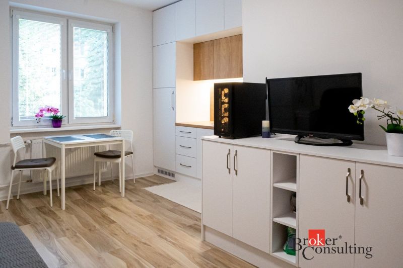 Studio apartment with a kitchenette, dining table, and wooden decor flooring.