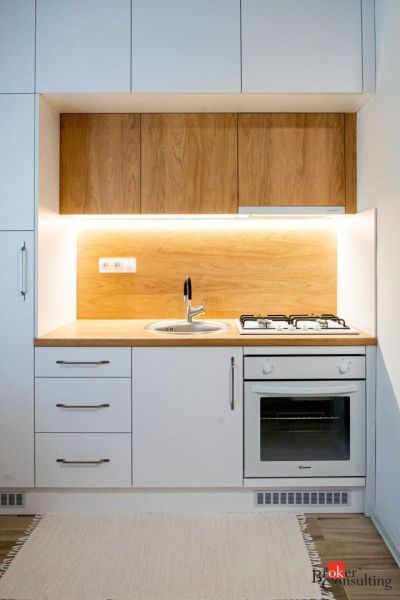 A kitchenette in a studio apartment with a wood decor, white cabinets, and a gas stove.