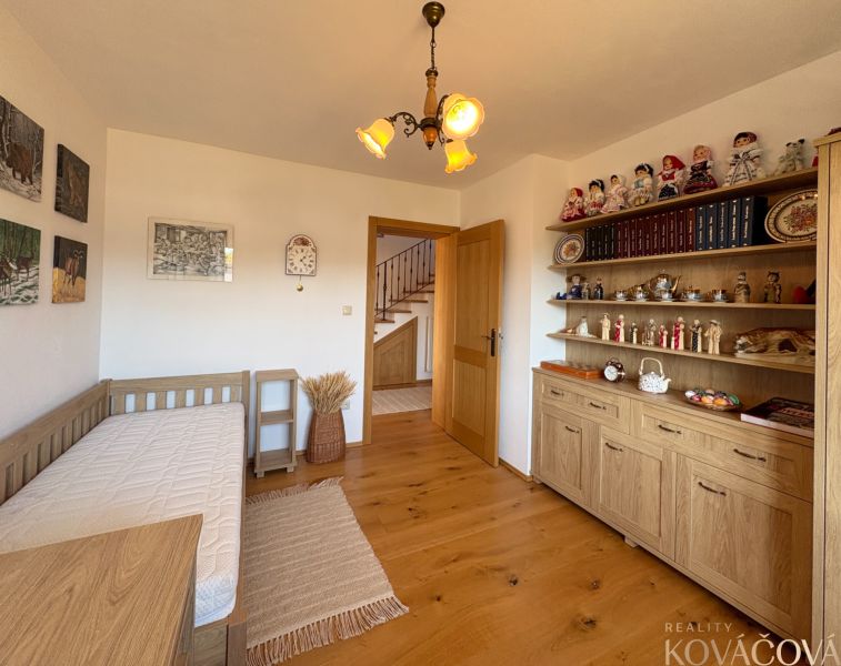 Interior of a family house with wooden decor, shelves with decorations, and a simple bed.