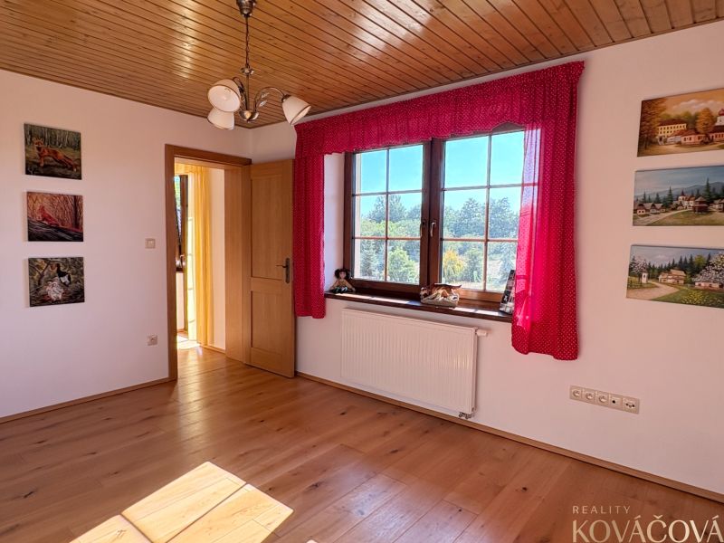 A room in a family house with a wooden decor floor, paintings, and a view of greenery.