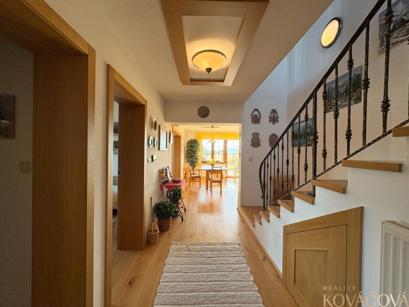 A hallway in a family house with a staircase, wall decorations, and a wooden-patterned floor.