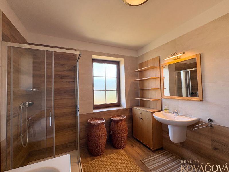 A bathroom in a family house with a wooden decor floor, a shower corner, and a sink.