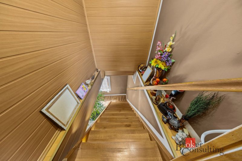 A staircase in a family house with a wooden decor floor, decoration, and flowers on the shelves.