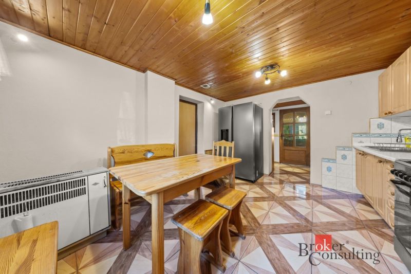 Dining room in a family house with a wooden ceiling, table and bench, tiled floor with a geometric pattern.
