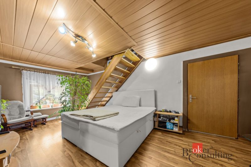 Bedroom in a family house with a bed, a plant, and stairs, floor with wood decor.